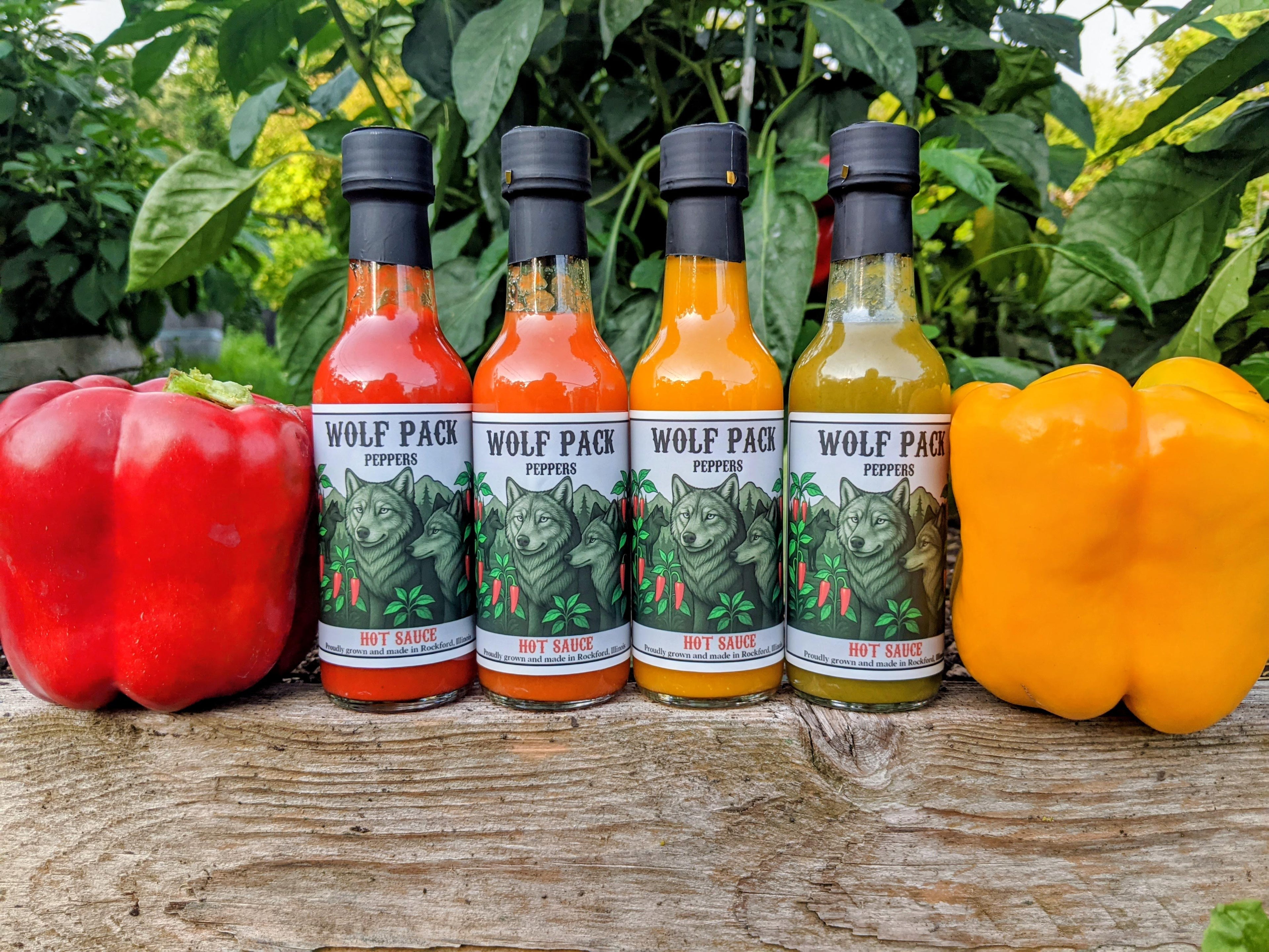 Four bottles of Wolf Pack Peppers hot sauce with peppers on a wooden surface